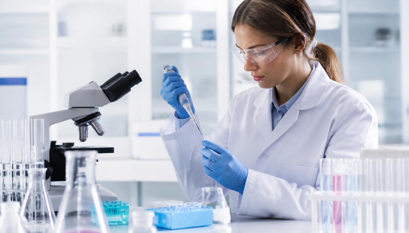 Researcher pipetting a sample beside a microscope in a laboratory